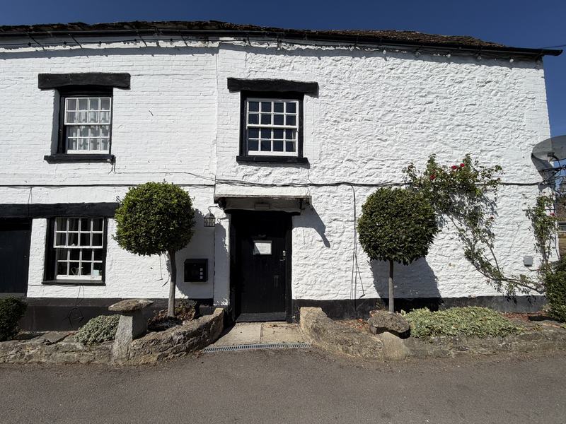 The whitewashed front of The Woodman Inn with black-framed sash windows