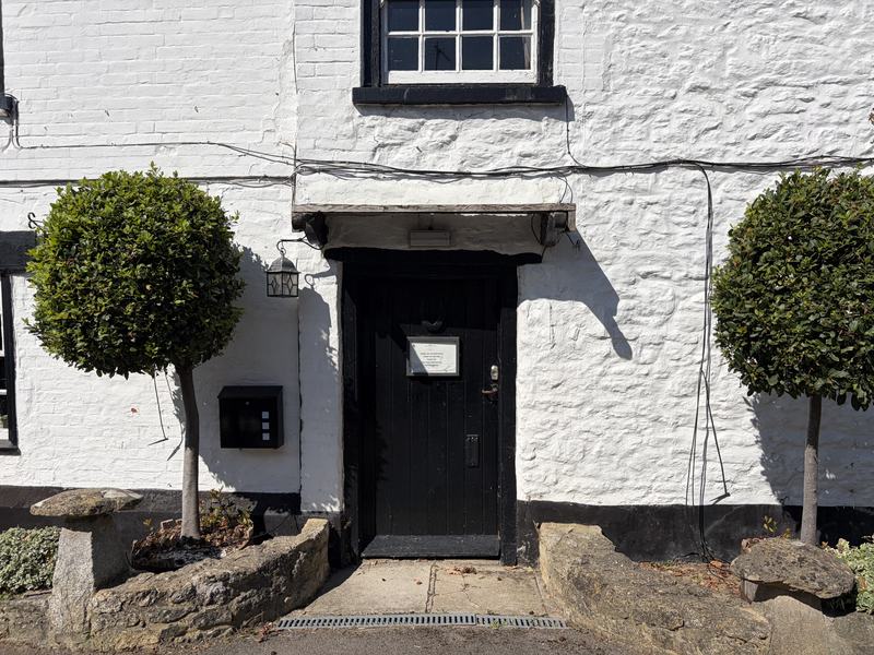 The black front door of the inn flanked by clipped bay trees