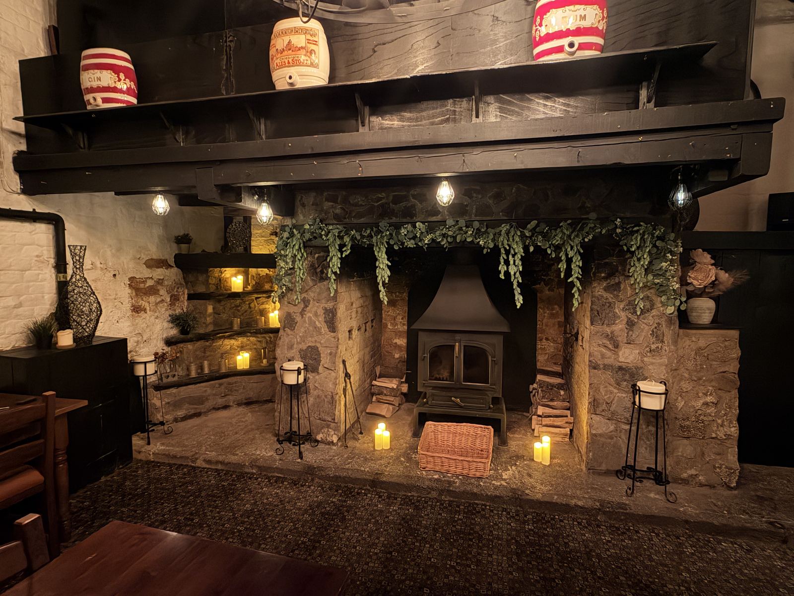 The inglenook fireplace lit by candles in the evening, with a log burner and gin barrels on the mantel