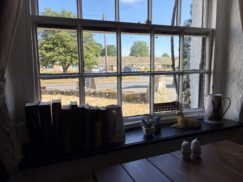 Books and jugs on a deep window sill looking out to the village